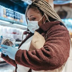 Image of a person wearing gloves and a face mask, carefully examining product information for sustainable choices