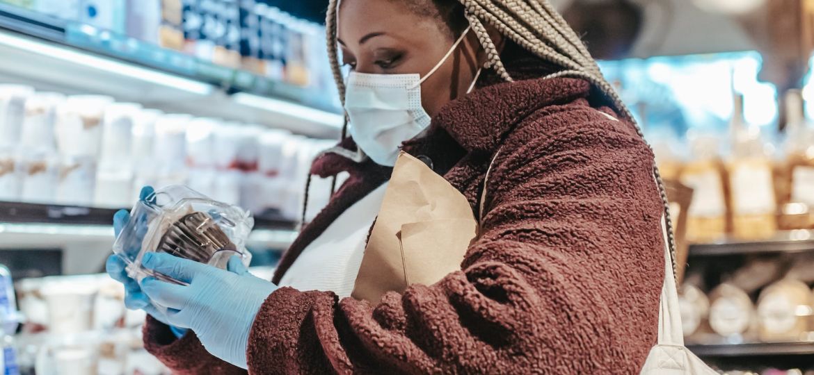 Image of a person wearing gloves and a face mask, carefully examining product information for sustainable choices