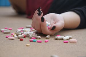 Person lying on the floor with a handful of assorted tablets