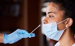 A person receiving a COVID-19 test at a drive-thru testing site, with a healthcare provider wearing protective gear.