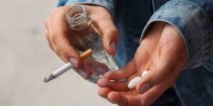 Substance abuse person holding a cigarette, bottle of alcohol, and tablets