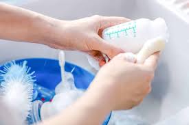 A set of baby feeding items, such as bottles and pacifiers, being scrubbed and rinsed.