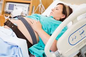 A woman lying on a hospital bed while having a CTG (Cardiotocography) test done. The woman is relaxed, with electrodes placed on her abdomen to monitor fetal heart rate and contractions. The CTG machine is visible nearby, displaying real-time data. The setting is a clinical environment, with soft lighting and medical equipment.