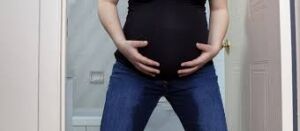 A pregnant woman wearing black pants, showing signs of rupture of membranes. The woman appears concerned, with a slight wet stain visible on the pants, indicating the leakage of amniotic fluid. The setting is calm, with soft lighting highlighting her posture and the situation.