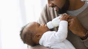 A father smiling as he bottle-feeds his baby, sharing a special moment together.