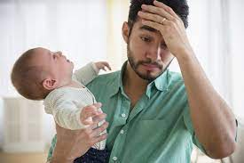 An overwhelmed father holding his head in frustration while cradling a crying baby.