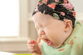 A baby coughing and appearing to choke, showing signs of discomfort and distress.