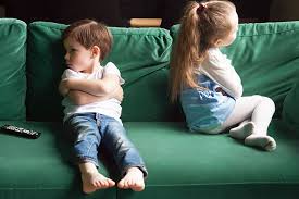 A brother and sister sitting apart on a couch, facing away from each other, indicating tension.