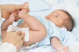A baby on a changing table, with a caregiver changing their nappy.