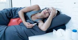 Sick person laying on a couch with a thermometer in their hand