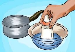 A hand submerging a bottle of breast milk into a bowl of warm water to bring it to the right temperature.