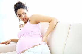 Side view of a pregnant woman leaning on her side, clutching her lower back and expressing discomfort.