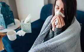 Person with Flu Sitting on Chair Wrapped in Blanket Blowing Nose in a Tissue