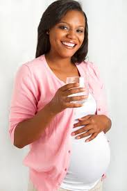 A glowing pregnant woman in a pink jacket, smiling as she holds a glass of water.