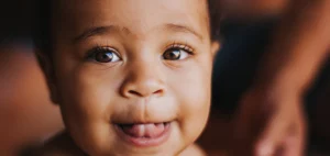 A close-up of a smiling baby with a joyful and content expression, showing a sense of satisfaction. The baby’s face is bright with happiness, and their eyes are sparkling. The background is soft and neutral, emphasizing the baby's joyful expression. The image conveys warmth, innocence, and a sense of peace.