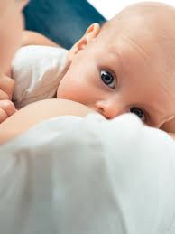 A baby gazing up lovingly at their mother while breastfeeding. The baby is latched on, with wide, curious eyes focused on the mother’s face. The mother’s expression is calm and nurturing as they share a peaceful bonding moment. The background is soft and intimate, highlighting the connection between mother and child.