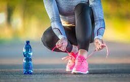 Prepping for fitness: Person tying shoelaces on the road with a water bottle nearby, emphasizing the importance of staying hydrated during physical activity.