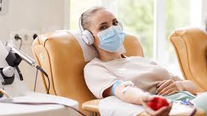 A person wearing a face mask sits comfortably on a chair, engaged in receiving treatment. Their contribution helps save lives and supports healthcare efforts.