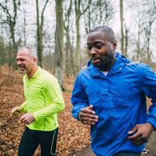 Two men jogging in the woods, engaging in exercise to promote overall well-being.