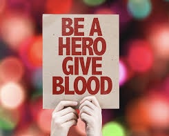 A person holds a sign encouraging others to give blood, emphasizing the importance of this life-saving act. Their advocacy helps raise awareness and inspire participation in donation efforts.