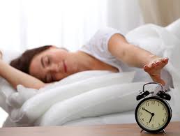 Alarm clock blaring as a sleepy individual attempts to silence it, highlighting the importance of eye exams for a clear wake-up.