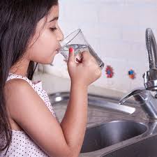 A young child holding a clear glass, taking a refreshing sip of water after regular eye exams. The innocence captured in the moment underscores the simple yet profound act of staying hydrated.