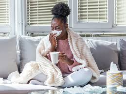 Woman with a Cold Sitting on a Couch, Wrapped in a Blanket, Blowing Her Nose with Tissue 