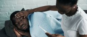 A concerned mother comforts her sick son, holding a thermometer in one hand while gently touching his forehead with the other.