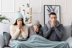 Family on sofa experiencing allergy symptoms, covered with a thick blanket.