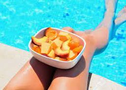 Poolside serenity: person enjoying fruits with feet in the water