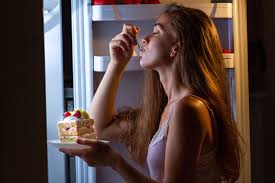 Person indulging in cake from the fridge as a midnight snack, highlighting late-night eating habits.