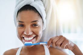 Woman smiling in front of a mirror, holding a toothbrush with toothpaste