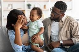 Couple seated on a chair; stressed new mother holding baby, showing signs of postpartum depression symptoms.