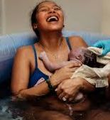 Woman experiencing epidural anesthesia appears joyful while seated in water and embracing her newborn.