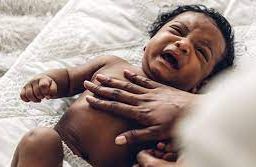 Person placing hand over crying baby in a calming gesture.