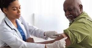 A female doctor carefully applying a dressing to a male patient’s arm after administering a vaccine. The doctor is focused and professional, wearing a white coat and gloves, while the patient sits calmly with his sleeve rolled up, showing a relaxed expression.